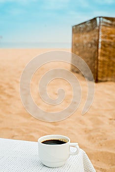 coffee espresso cup with ocean , beach and seascape. Blue sky, white sand, woven zonik, wooden beach chair. Sea vacations. The