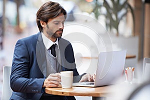 Coffee-fueled concentration. A handsome businessman working on his laptop at a coffeeshop.