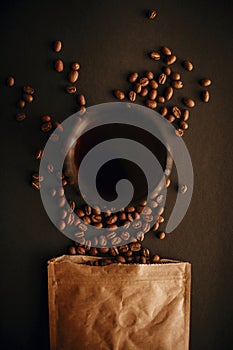 Coffee in glass cup and coffee beans scattered from paper pack on black background.Flat lay, Dark moody image. Fresh aromatic