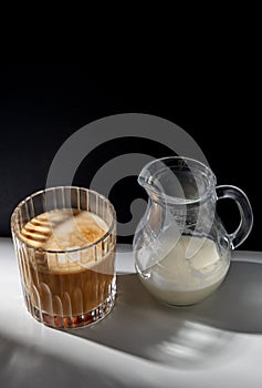 coffee in glass and jug of milk or cream on table