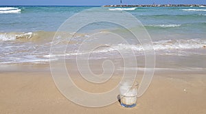 Coffee glass stands in wet sand near sea waves