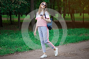 Coffee on go. Beautiful young woman in sunglasses holding coffee cup and smiling while walking