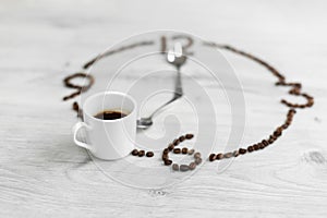 Coffee grains folded in the form of a clock on a wooden background. Instead of the number 7, a cup of coffee, which means it`s