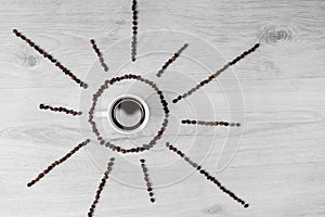 Coffee grains folded in the form of the sun on a wooden background. In the middle is a cup of coffee, meaning it`s time to drink