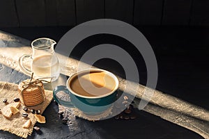 Coffee in a green cup with fresh milk and breakfast bread on a black wooden table in a coffee shop with a background of warm