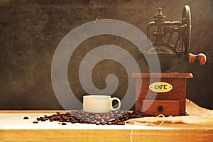 Coffee grinder and some bean with a cup on a wooden table.