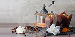 Coffee grinder, two muffins, aroma coffee grains and flowers of azalia on black stone.