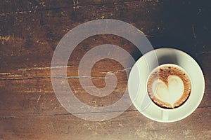 Coffee with heart pattern in a white cup on wooden background