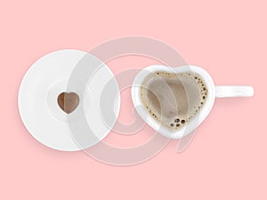 coffee in heart shape cup and tiny heart shape chocolate on white ceramic saucer isolated on pastel pink background