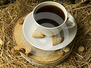 Coffee and a heart shaped cookie on a wooden saw on a black background. Breakfast for her on Valentine`s Day. Cookies