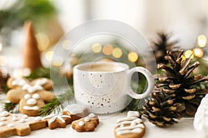 Coffee, homemade gingerbread cookies, pine cones decorations and warm lights on white  table