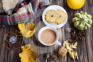 Coffee or hot chocolate cup on autumn setting top view with dried leaves, cosy blanket, cookies, fall decorations