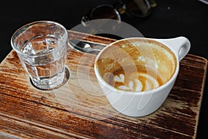 Coffee with latte art is drunk. Ceramic cup and glass of water on brown wooden table in cafe