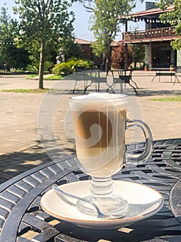 Coffee latte or cappuccino with milk foam in a tall glass on a wrought iron table in a street summer cafe