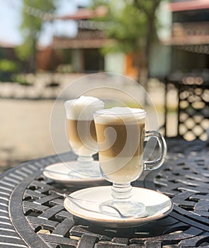 Coffee latte or cappuccino with milk foam in a tall glasses on a wrought iron table in a street summer cafe