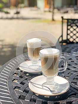 Coffee latte or cappuccino with milk foam in a tall glasses on a wrought iron table in a street summer cafe