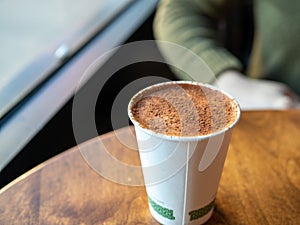 Coffee latte covered in cocoa powder in compostable cup on table in cafe