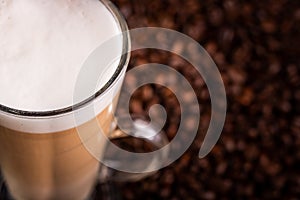 Coffee latte with frothy milk in tall glass, on coffee beans