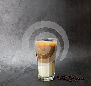 Coffee latte is layered with milk. Cold caffeine drink on a transparent glass and roasted coffee beans on black marble background