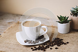 Coffee latte in white cup, coffee beans on sackcloth napkin. Closeup