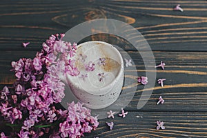 Coffee with lilac petals and blooming branch on dark wooden background with space for text