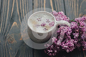 Coffee with lilac petals and blooming branch on dark wooden background with space for text