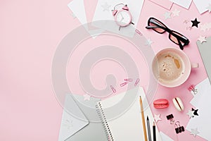 Coffee, macaron, alarm clock, office supply and notebook on pink pastel table top view. Flat lay. Woman blogger working desk.