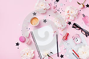 Coffee, macaroons, alarm clock, office supply, peony flowers and notebook on pink pastel table top view. Flat lay style.