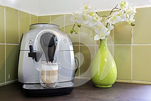 Coffee machine maker with a latte macchiato in cozy decorative home with green wall and flowers. home made coffee
