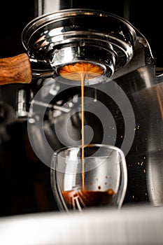 Coffee machine pouring hot espresso in double wall glass from bottomless naked portafilter.