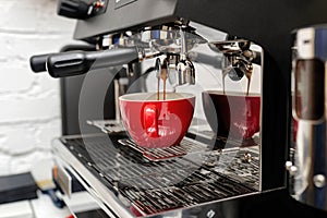 Coffee machine preparing fresh coffee and pouring into red cups at restaurant