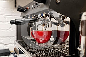 Coffee machine preparing fresh coffee and pouring into red cups at restaurant