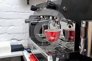 Coffee machine preparing fresh coffee and pouring into red cups at restaurant
