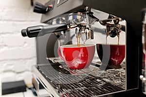 Coffee machine preparing fresh coffee and pouring into red cups at restaurant