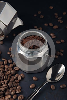 Coffee maker with ground coffee, coffee beans and metal spoon on dark textured background