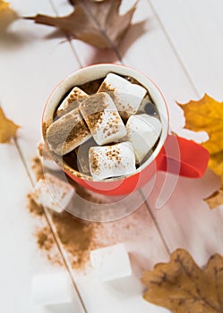 Coffee and marshmallows in a red cup and yellow leaves. Cozy time with a cup of coffee in the fall season. Hot drink