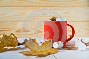 Coffee and marshmallows in a red cup and yellow leaves. Cozy time with a cup of coffee in the fall season. Hot drink