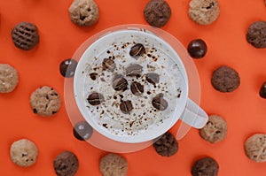 Coffee with milk and coffee beans on orange background with cookies and chocolate balls. Flat lay