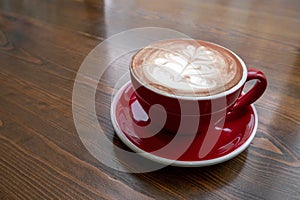 coffee with milk and foam pattern poured into a red ceramic mug on a vintage wooden table in the coffee shop