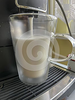 Coffee with milk poured from a coffee machine into a transparent, double-walled thermal mug