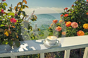Coffee with milk on the terrace surrounded by beautiful blooming roses