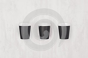 Coffee mockup - set of three small blank black paper cups with white caps on white wood board, top view.