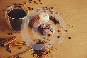 Coffee moody image. Glass cup with fresh coffee and roasted beans,ground coffee on spoon, macarons, chocolate, cinnamon on brown