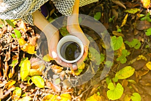 Coffee mug in autumn wood. Woman holding cup with hot drink. Cosy mood. Red and yellow leaves. Beautiful nature