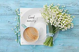 Coffee mug with bouquet of flowers lily of the valley and notes good morning on turquoise rustic table from above