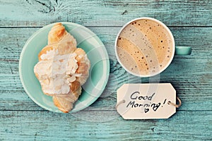 Coffee mug with croissant and notes good morning on turquoise rustic table from above, cozy and tasty breakfast photo