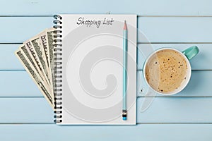 Coffee mug and notebook with shopping list and cash money dollar on blue rustic table