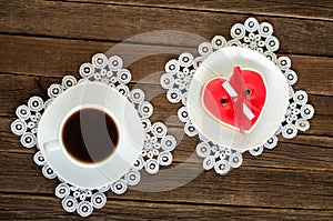 Coffee mug, saucer with red heartshaped gingerbread on the old wooden background.