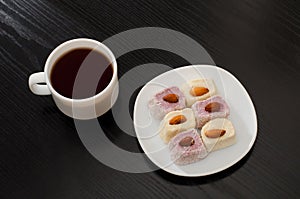 Coffee mug, saucer with Turkish Delight on a black table, top view