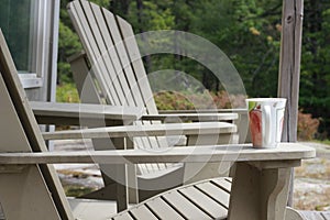 A coffee mug sitting on a Muskoka chair on a dock. Lake and cottages in the background - horizontal orientation. Perfect for